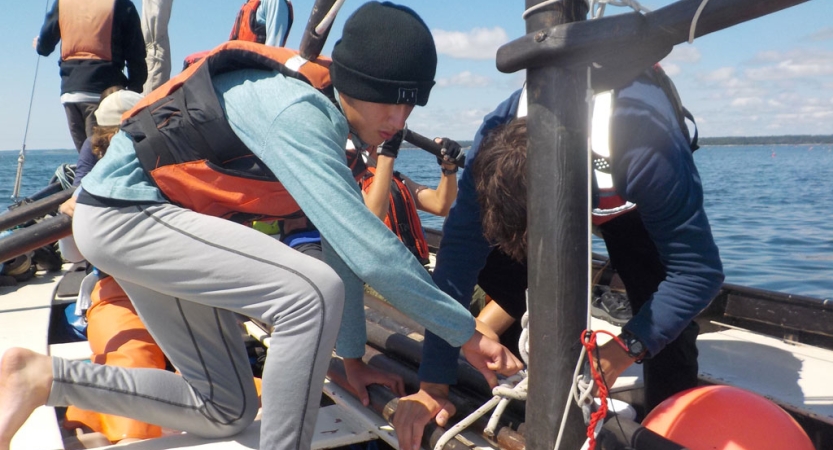 A group of people wearing life jackets work on a sailboat. 